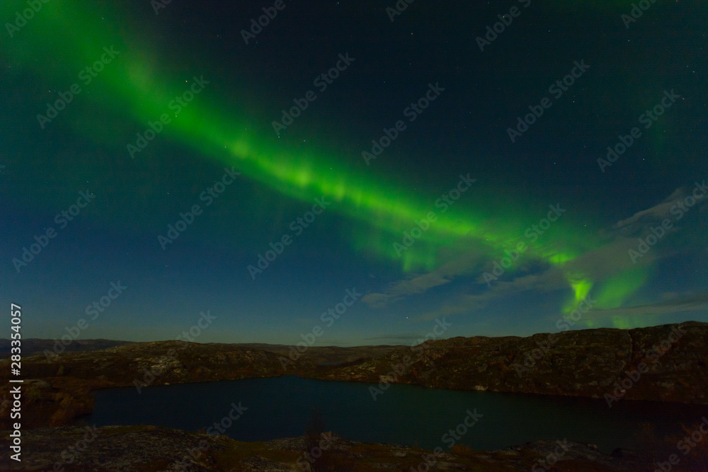 Northern lights, aurora in the sky above the hills and rocks at night.
