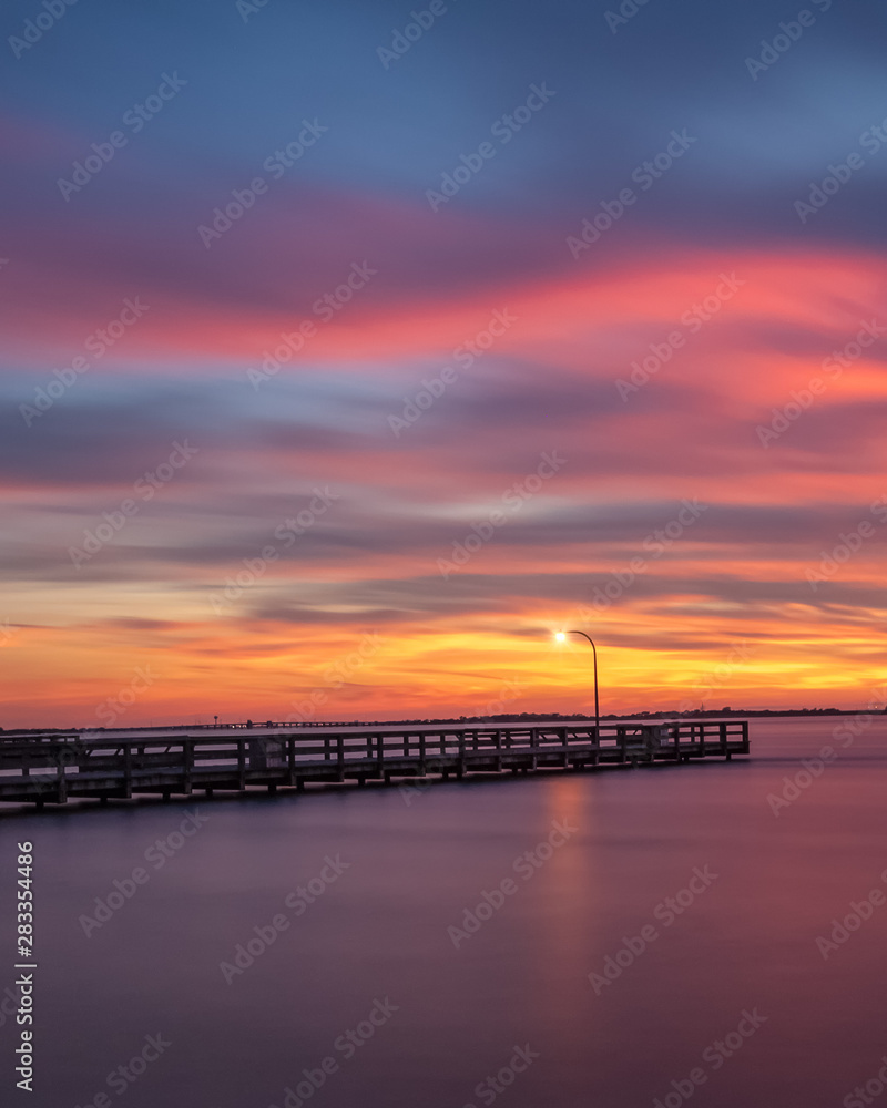 Vibrant colors light up the sky just after sunset over a long fishing pier. Jones Beach, Long Island New York