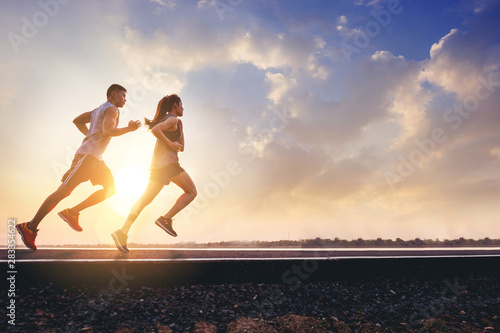 Fototapeta Naklejka Na Ścianę i Meble -  Young couples running sprinting on road. Fit runner fitness runner during outdoor workout with sunset background