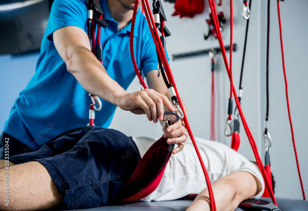 Physiotherapy. Suspension training therapy. Young man doing fitness traction therapy with suspension-based exercise training system.