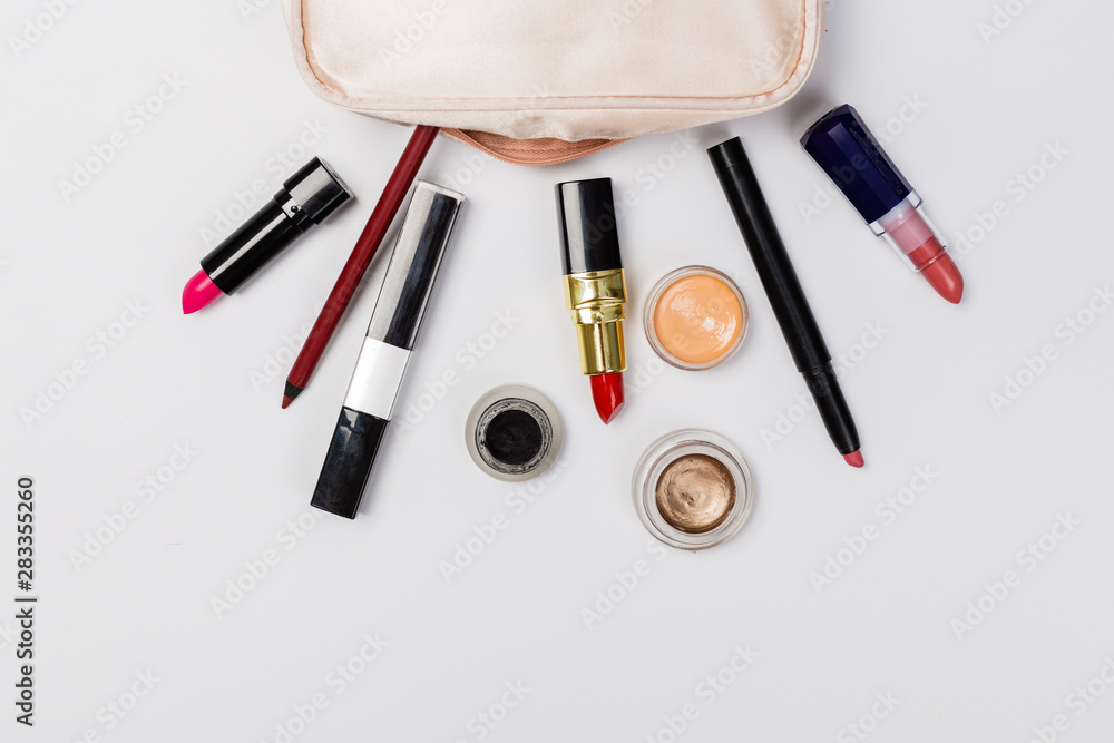 A pink makeup bag with cosmetic beauty products spilling out on to a light background, with empty space at side A pink makeup bag with cosmetic beauty products spilling out on to a light background, with empty space at side