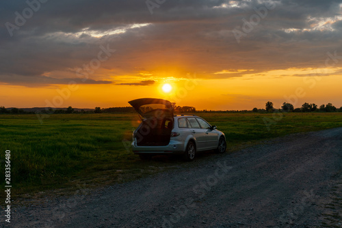 A car parked on a field at sunset in a rural landscape