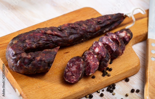 French tasty slicing dry-cured sausage with liver at wooden desk