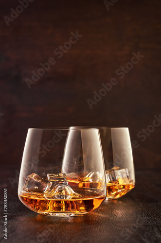 Two crystal glasses of whisky with ice on a wooden table.