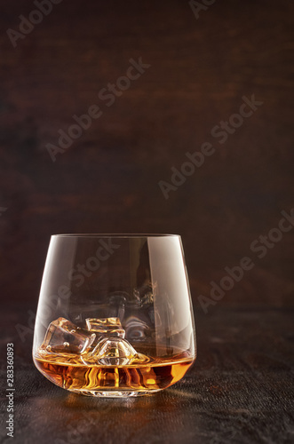 A crystal glass of whisky with ice on a wooden table.