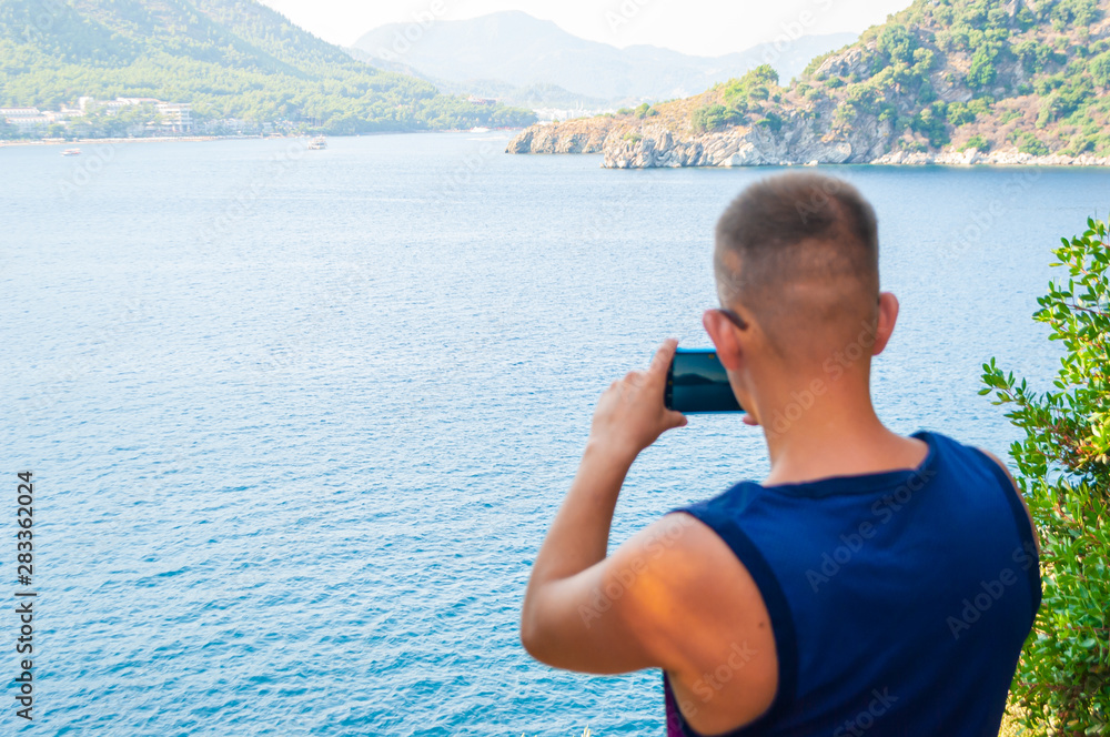 Young caucasian tourist taking photo on his celephone of mountain and sea in travel