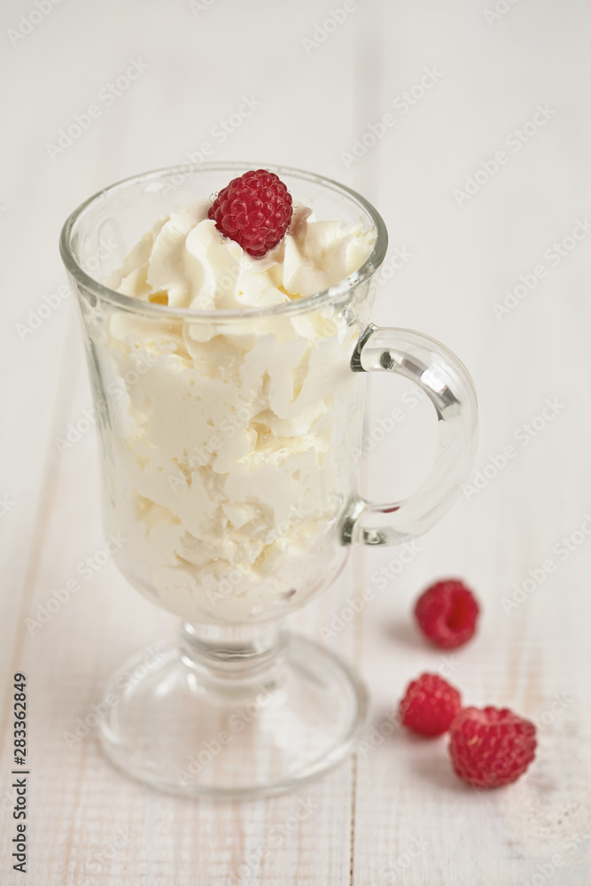 Glass with whipped cream and raspberries on a white table Glass with whipped cream and raspberries on a white table