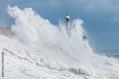 Huge ocean waves crashing into a sea wall and lighthouse (Porthcawl, South Wales, UK)