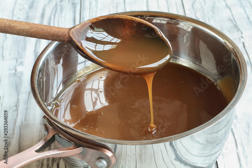 Obraz na płótnie Wooden spoon dripping caramel sauce into a pan