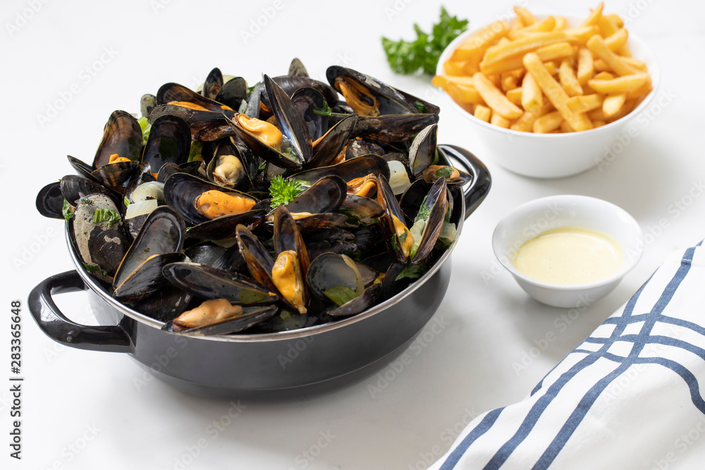 Belgian mussels with potato fries and sauce on white marble table Belgian mussels with potato fries and sauce on white marble table