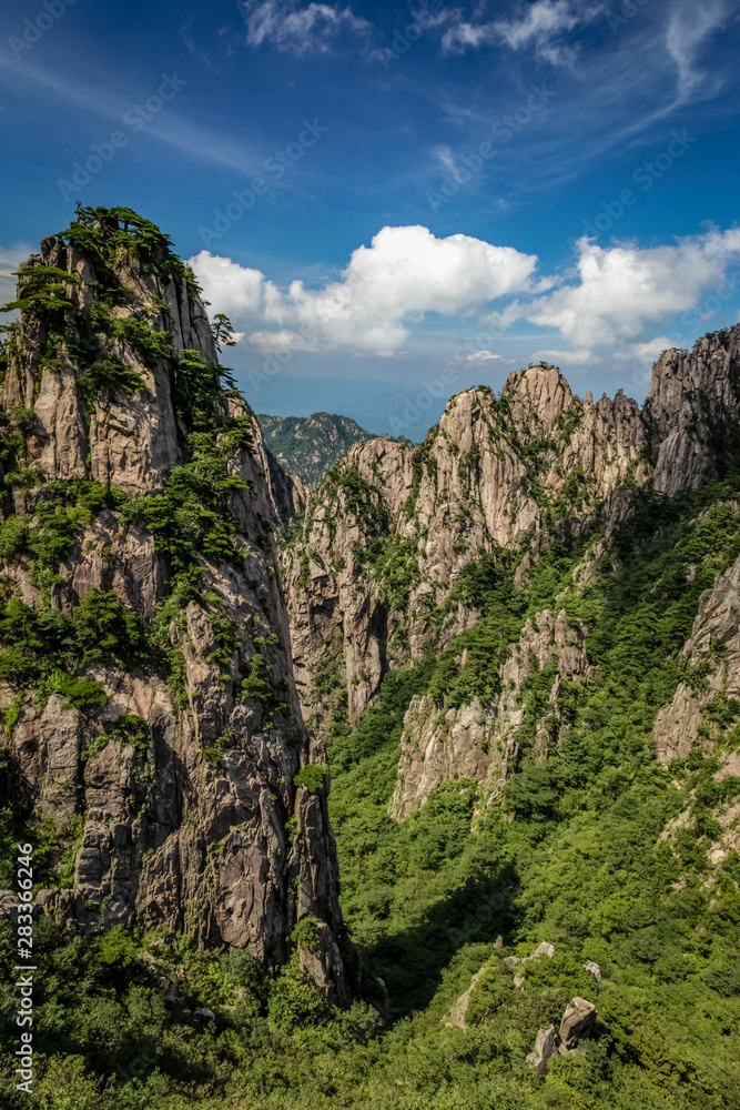 Steep mountain pinnacle on the left casting a short shadow on the green valley in Huang Shan (黄山, Yellow Mountains) China Steep mountain pinnacle on the left casting a short shadow on the green valley in Huang Shan (黄山, Yellow Mountains) China