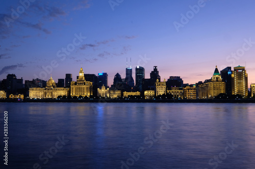 Sunset blue hour of The Bund in Shanghai. Golden illuminated western buildings on the bank of Huangpu River. Long exposure peaceful river. Wide angle