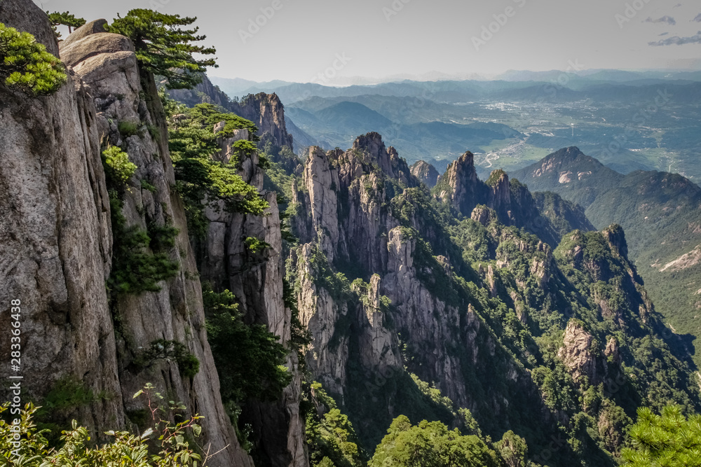Steep vertical stone on the left leading to a valley and city in the far distance on the right in Huang Shan (黄山, Yellow Mountains) China