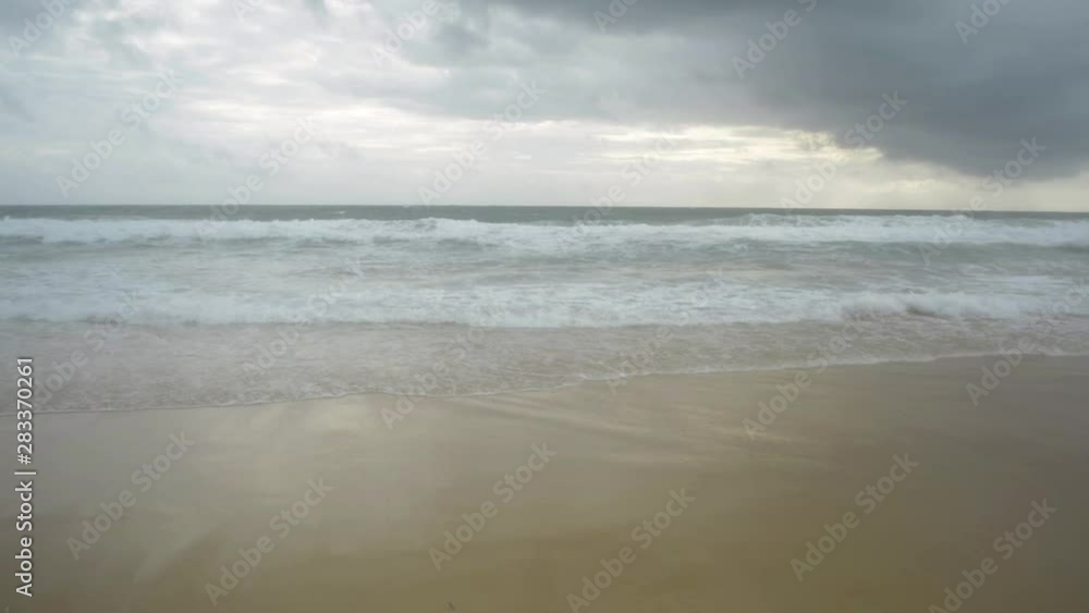 Scenery of tropical sandy beach with foam formed by waves breaking on a seashore and rain clouds in the sky at karon beach, Phuket, Thailand. Scenery of tropical sandy beach with foam formed by waves breaking on a seashore and rain clouds in the sky at karon beach, Phuket, Thailand.