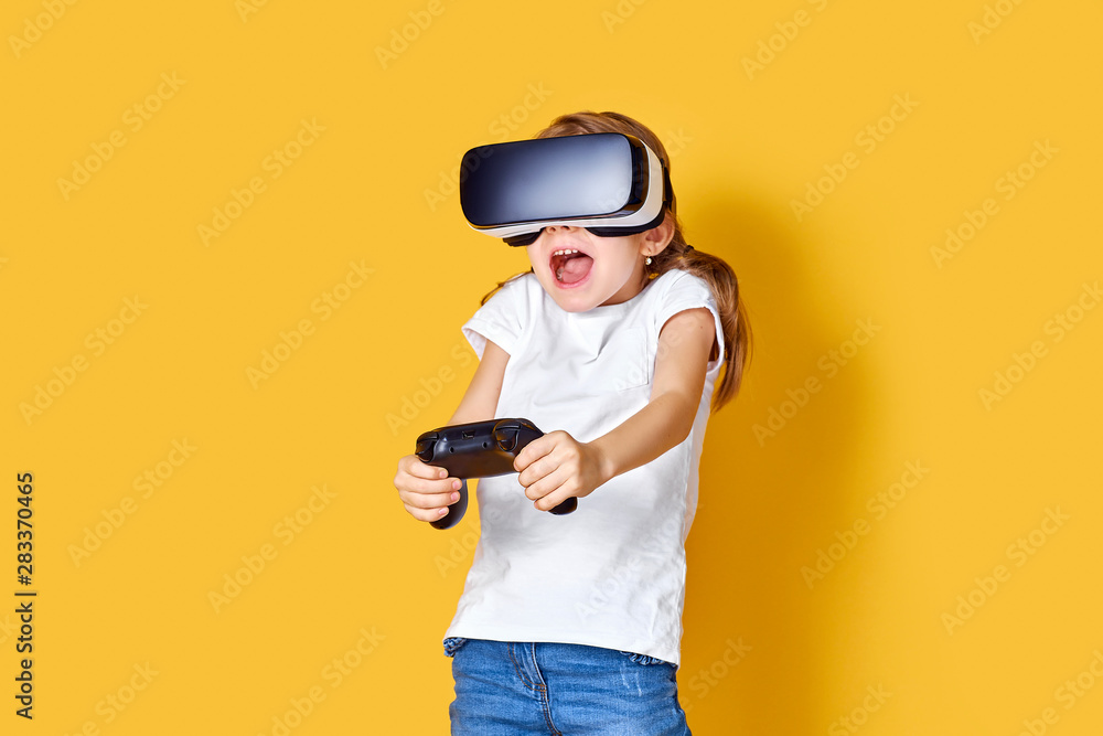 Girl experiencing VR headset vs joystick game on yellow background. Surprised emotions on her face. Child using a gaming gadget for virtual reality. Futuristic goggles at young age. Virtual technology Girl experiencing VR headset vs joystick game on yellow background. Surprised emotions on her face. Child using a gaming gadget for virtual reality. Futuristic goggles at young age. Virtual technology