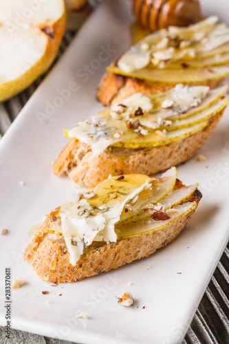 Appetizer bruschetta with pear, honey, walnut and blue cheese on white plate