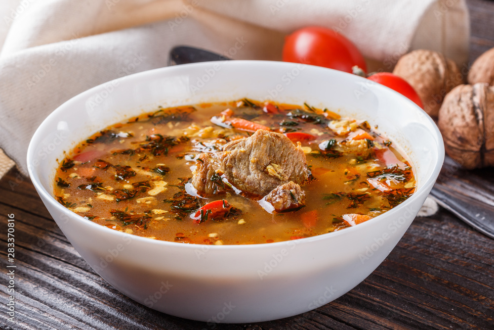 Georgian soup. Kharcho with rice, tomato, beef, garlic and herbs in bowl on wooden table Georgian soup. Kharcho with rice, tomato, beef, garlic and herbs in bowl on wooden table
