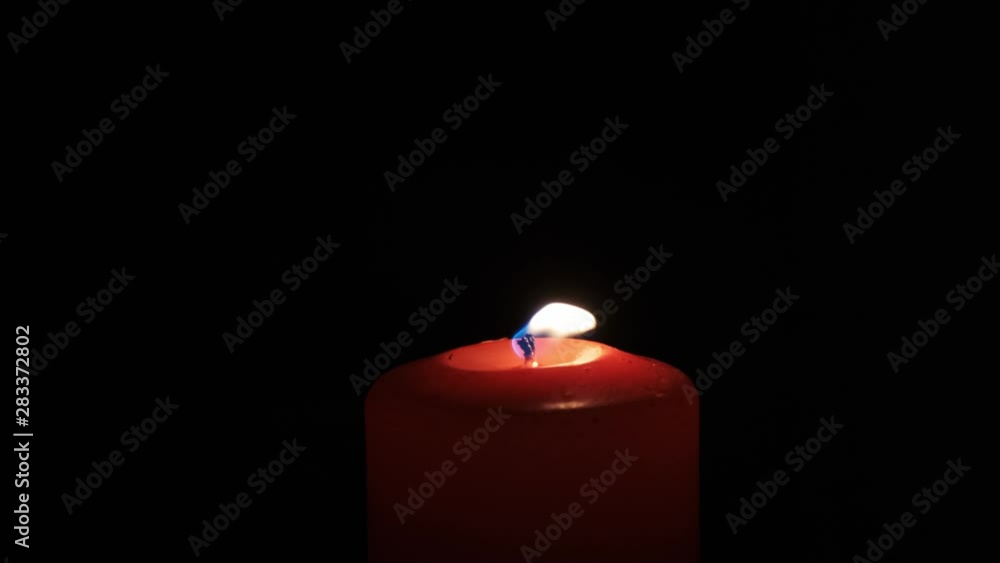 Burning red candle on black background.