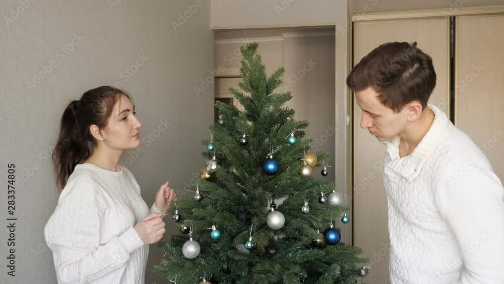 handsome young man and pretty lady in white sweaters hold colorful toys decorating artificial christmas tree close view handsome young man and pretty lady in white sweaters hold colorful toys decorating artificial christmas tree close view