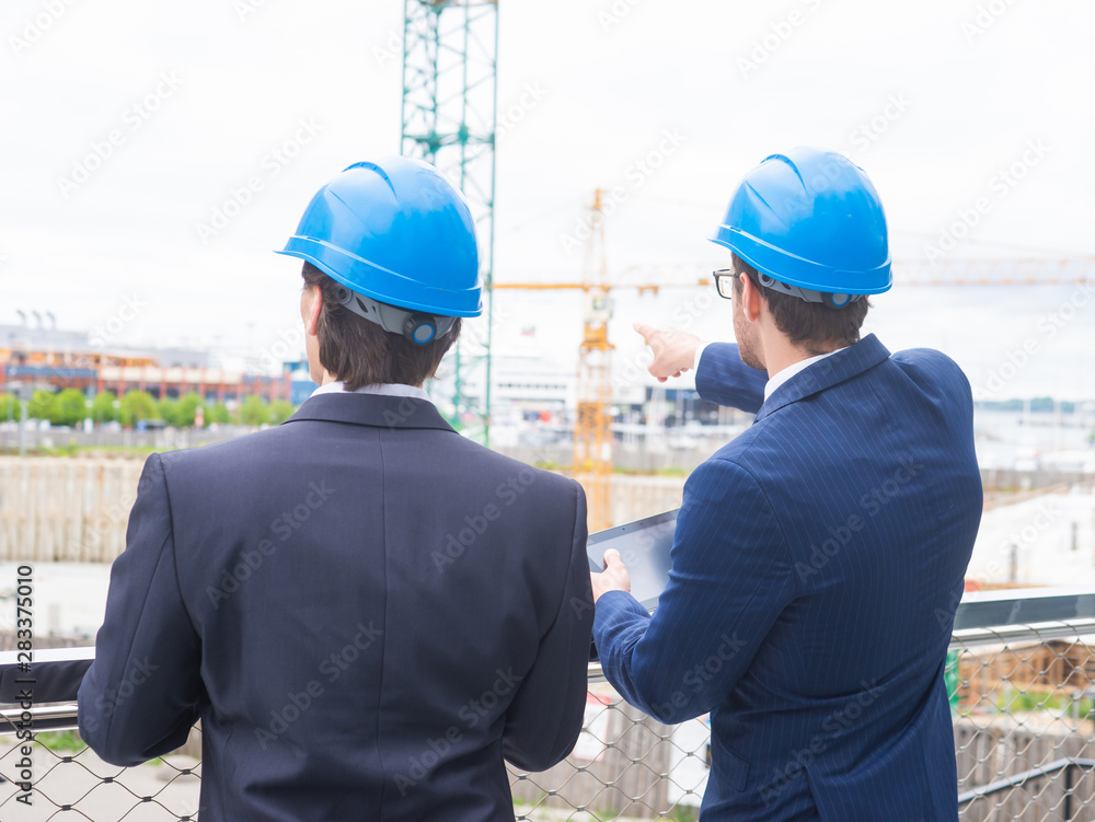 Real estate developers in helmets. New office construction. Confident business men and architect talking in front of modern office building. Real estate developers in helmets. New office construction. Confident business men and architect talking in front of modern office building.