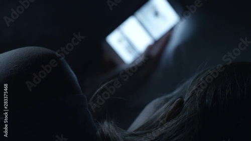 A woman scrolling on her mobile phone in bed at night. The bright blue screen light illuminating her face.