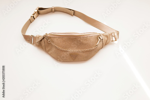 Glamorous women's belt bag of golden color on a white isolated background. Fashion handbag with a gold chain.