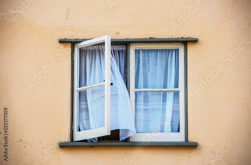 Canvas Print Open casement window in old stucco house with white gauze sheer curtains blowing