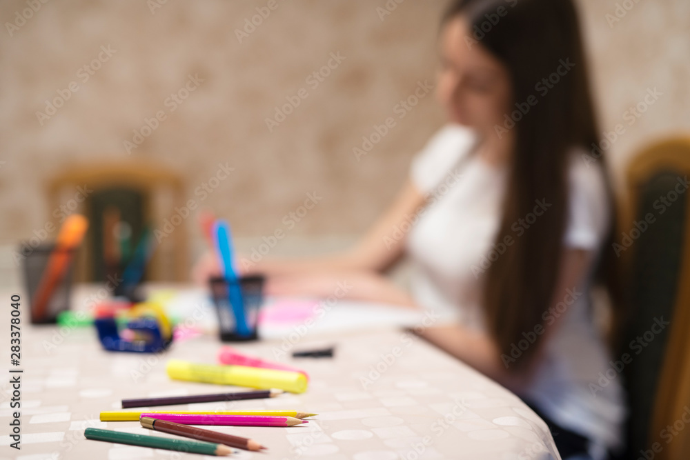 Focus on pencils and pans while teenage girl doing her homework and studying for school in background. Education and learning concept. Focus on pencils and pans while teenage girl doing her homework and studying for school in background. Education and learning concept.