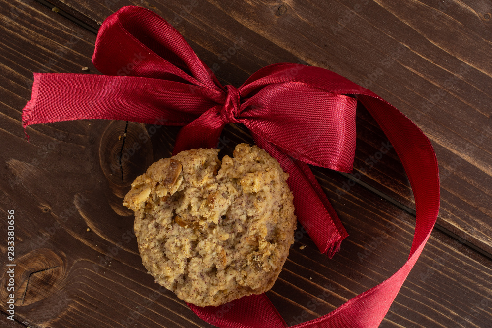 One whole oat crumble biscuit with crimson ribbon flatlay on brown wood One whole oat crumble biscuit with crimson ribbon flatlay on brown wood