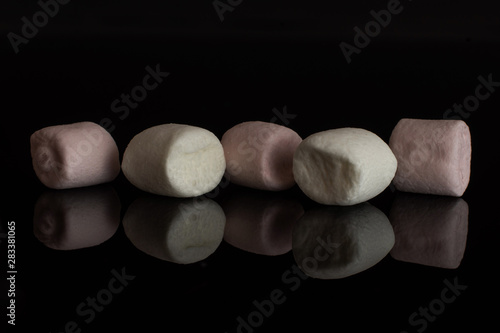 Group of five whole pink and white sweet fluffy marshmallow isolated on black glass