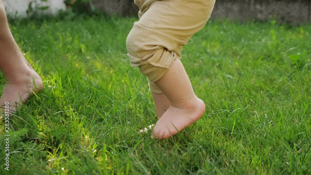 man and toddler son in beige pants bare feet walk on fresh green grass on sunny day close low angle shot slow motion man and toddler son in beige pants bare feet walk on fresh green grass on sunny day close low angle shot slow motion