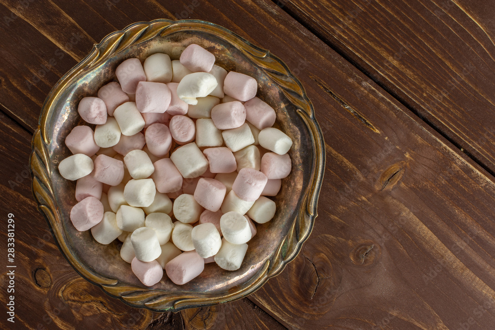 Lot of whole sweet fluffy marshmallow in old iron bowl flatlay on brown wood Lot of whole sweet fluffy marshmallow in old iron bowl flatlay on brown wood
