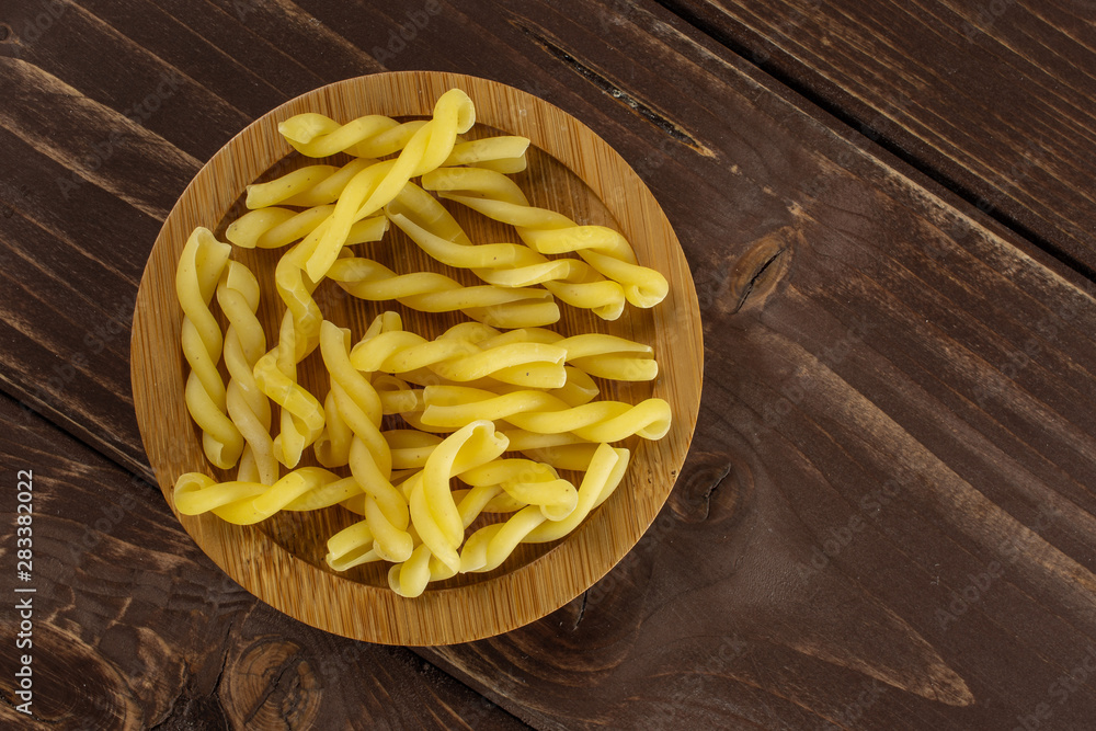 Lot of whole raw pasta gemelli on bamboo plate flatlay on brown wood