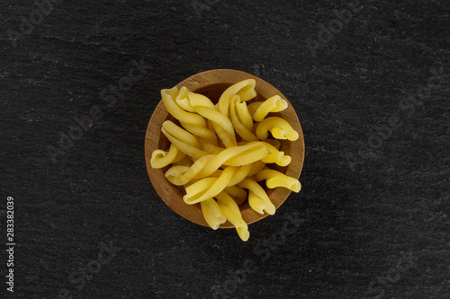 Lot of whole raw pasta gemelli in wooden bowl flatlay on grey stone
