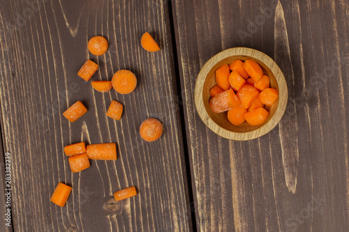 Lot of pieces of stale  orange stale baby carrot baby in wooden cup flatlay isolated on brown wood