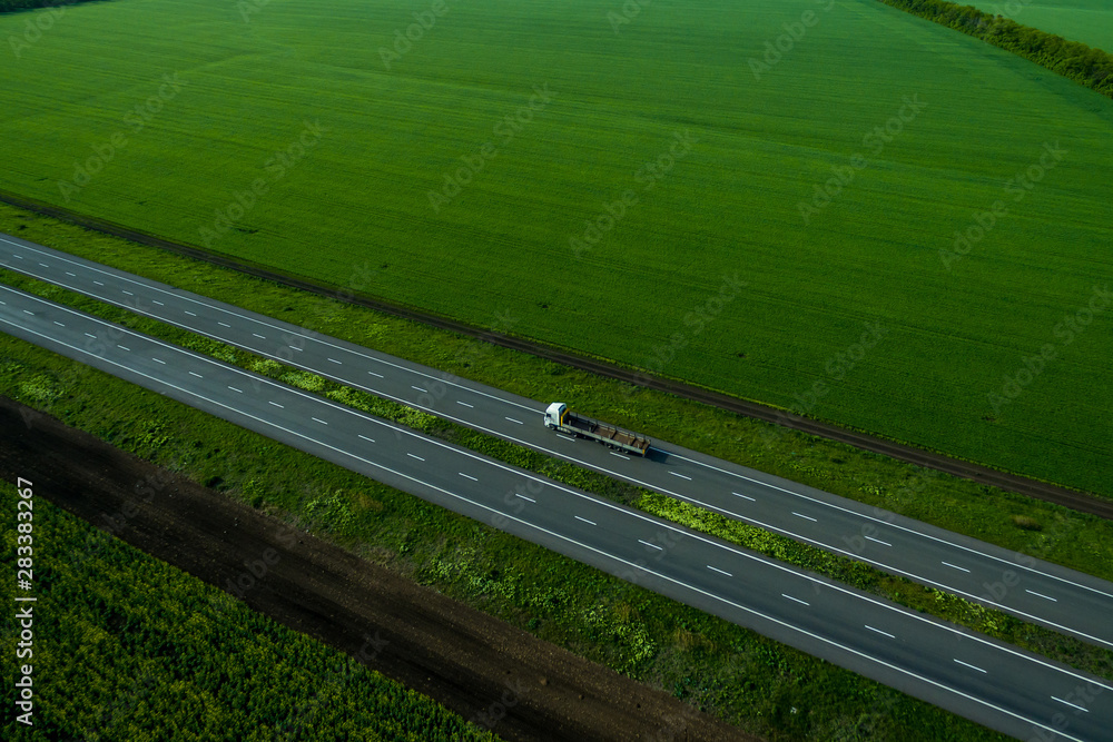 white truck driving on asphalt road along the green fields. seen from the air. Aerial view landscape. drone photography.  cargo delivery