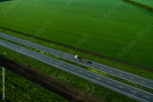 white truck driving on asphalt road along the green fields. seen from the air. Aerial view landscape. drone photography. cargo delivery