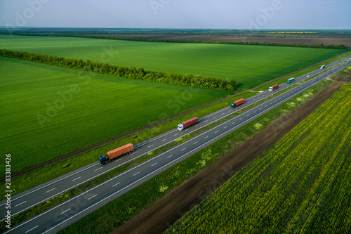 truck convoy on the higthway sunset. cargo delivery driving on asphalt road along the green fields. seen from the air. Aerial view landscape. drone photography.