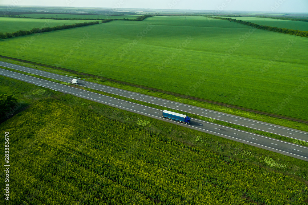 Blue truck driving on asphalt road along the green fields. seen from the air. Aerial view landscape. drone photography.  cargo delivery