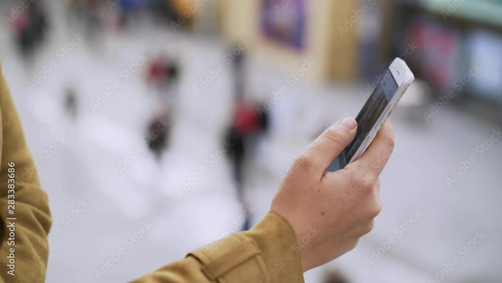 Young woman standing on train station with cellphone in hands. Close-up view female hand holding phone, using for communication and waiting our train at blurred background with walking people Young woman standing on train station with cellphone in hands. Close-up view female hand holding phone, using for communication and waiting our train at blurred background with walking people