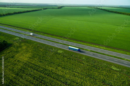 Blue truck driving on asphalt road along the green fields. seen from the air. Aerial view landscape. drone photography. cargo delivery