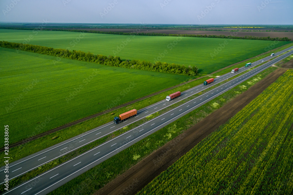 trucks on the higthway sunset. cargo delivery driving on asphalt road along the green fields. seen from the air. Aerial view landscape. drone photography.