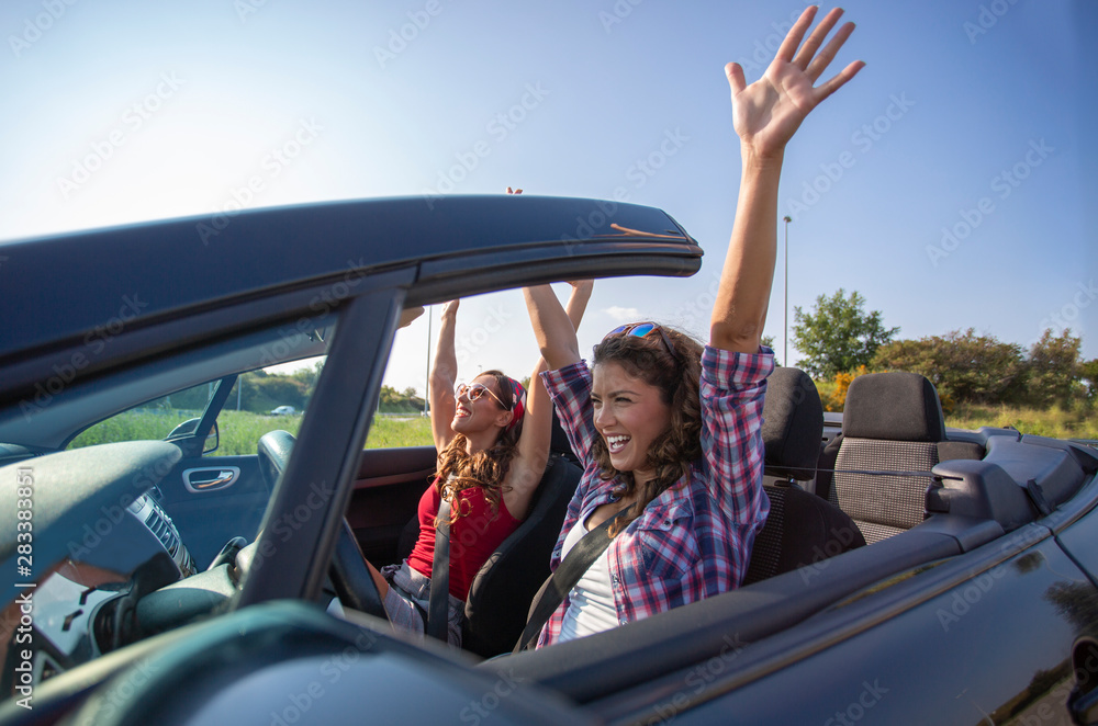 Φωτογραφία Two beautiful young women driving in a convertible with hands in the air
