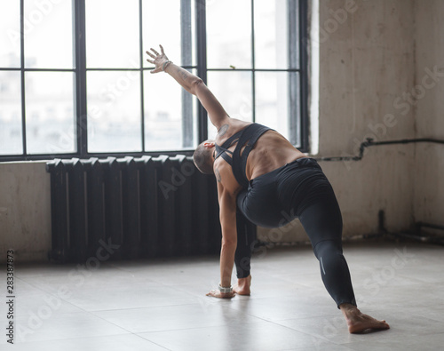 muscular female in sportswear doing yoga execise near window in loft interior