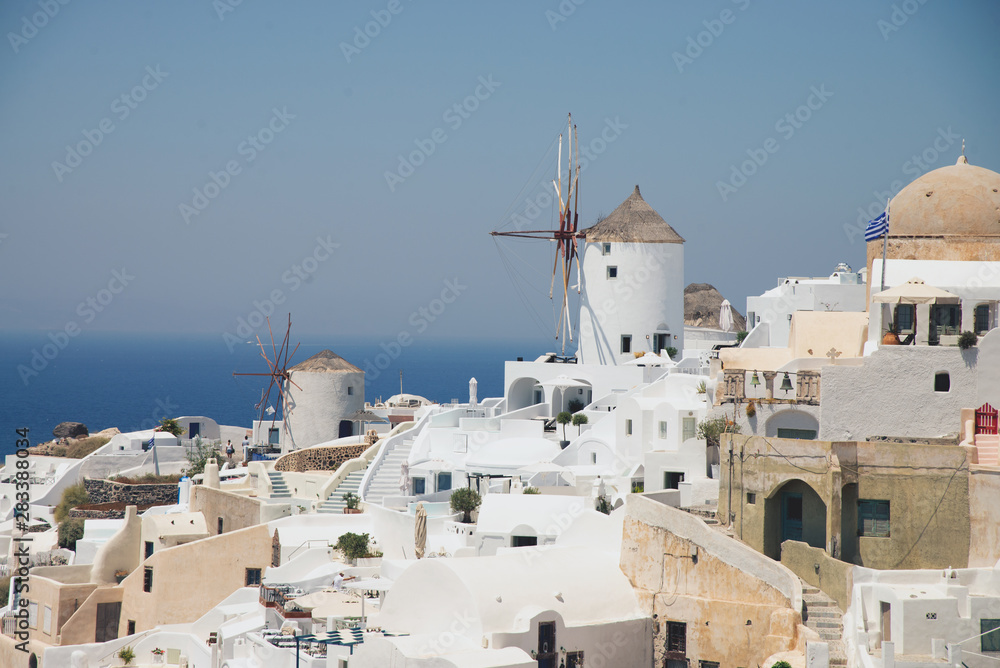 Panorama with characteristic white houses of Oia in Santorini volcanic island of the Aegean Sea in Greece. Gulf of the caldera with hotels with swimming pools, mills turned into restaurants