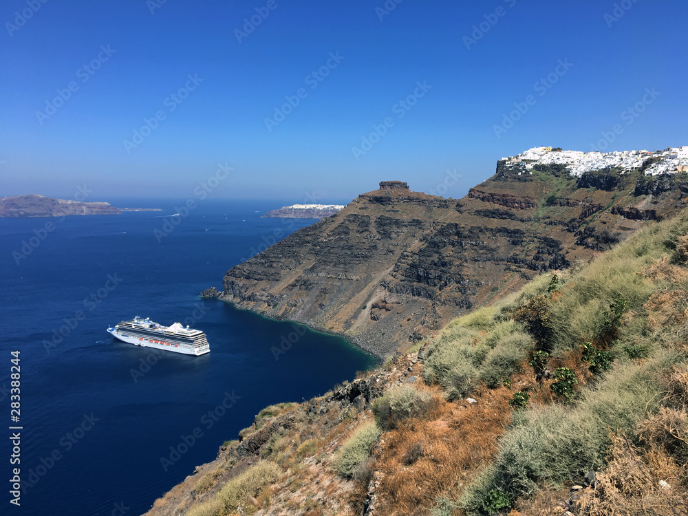 Panorama with the cliff of volcanic rocks of Oia in Santorini island of the Aegean sea in Greece. Gulf of the caldera with cruise ship and Thirasia islands.