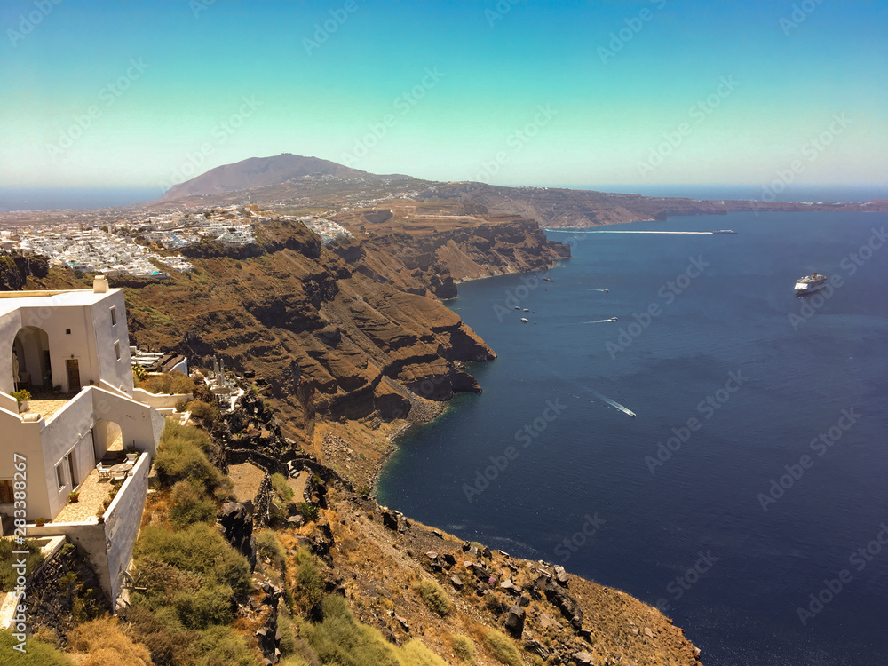 Panorama with the cliff of volcanic rocks of Oia in Santorini island of the Aegean sea in Greece. Gulf of caldera with cruise ships and islands of Nea and Palea Kameni.