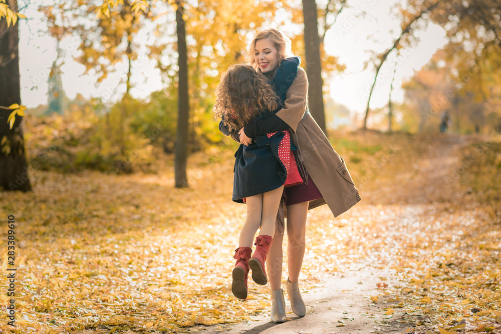 Portrait of smiling mother and daughter with leaves in hands lying on yellow grass. Beautiful family resting in the park. Autumn portrait. Portrait of smiling mother and daughter with leaves in hands lying on yellow grass. Beautiful family resting in the park. Autumn portrait.