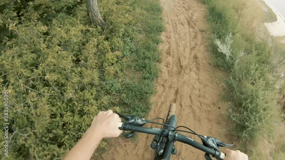 A young man rides a bicycle on the high bank of the river. You can see the hands and handlebars of the bike. Under the wheels of sand. Close-up . Atmospheric video A young man rides a bicycle on the high bank of the river. You can see the hands and handlebars of the bike. Under the wheels of sand. Close-up . Atmospheric video
