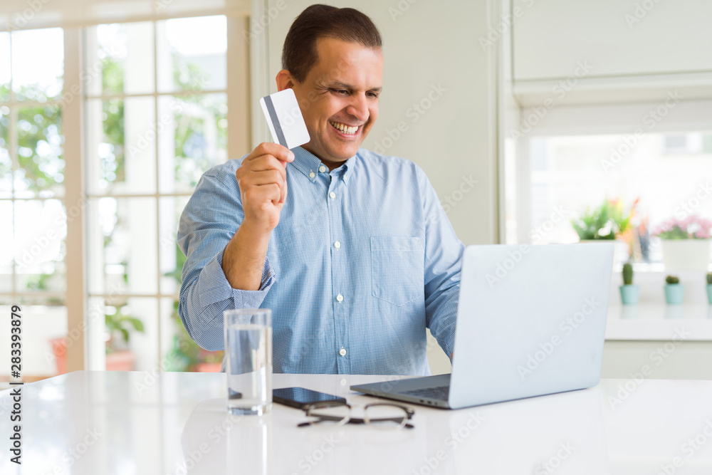 Middle age man showing credit card while using laptop
